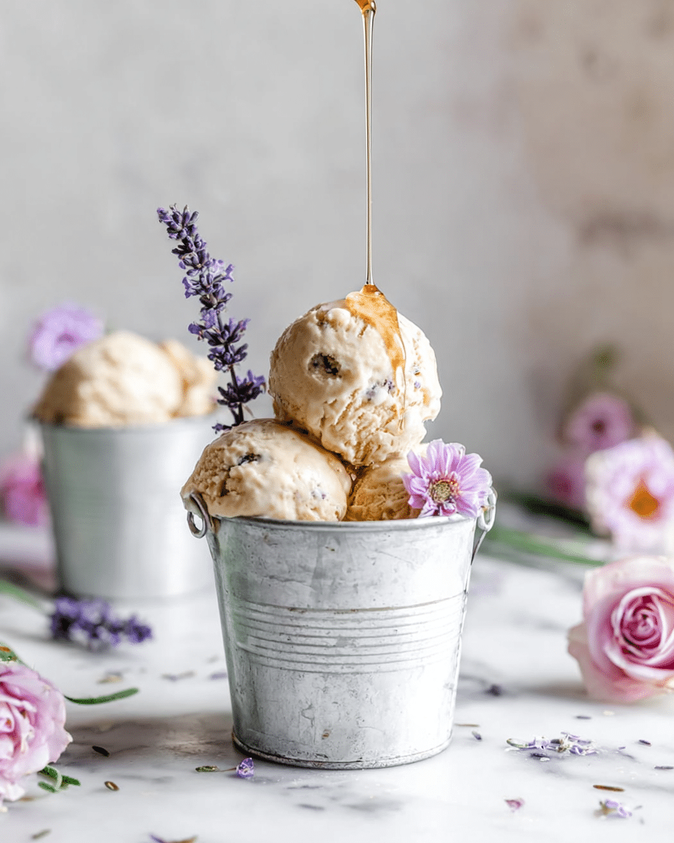 The image shows a small white metal bucket filled with three scoops of light beige ice cream with visible small dark bits, placed on a white marbled surface. On top of the ice cream, there is a small pink flower and a purple lavender sprig on the side of the bucket. Above the ice cream, a thin stream of honey or syrup is being poured down. In the soft-focused background, there is another similar bucket with ice cream and a small flower. Around the buckets, there are soft pink roses and lavender flowers scattered on the white marbled surface. photo taken with an iphone --ar 4:5 --v 7