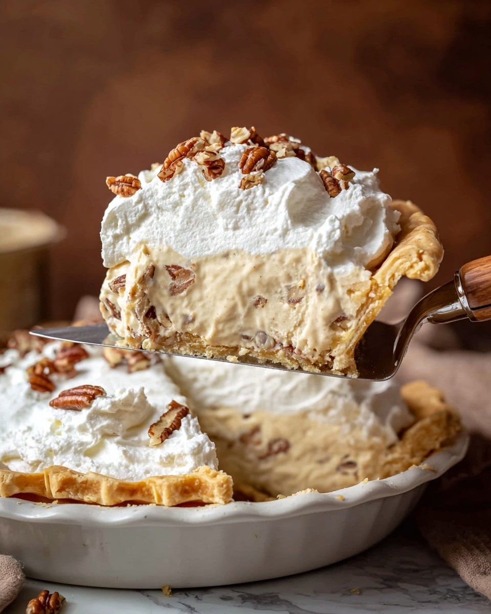 The image shows a slice of a creamy pie being lifted from a larger pie in a white pie dish. The pie has three layers: a golden-brown flaky crust at the bottom with a crimped edge, a thick light beige creamy filling with visible pecan pieces inside, and a thick, smooth white whipped topping crowned with small chopped pecan bits scattered on top. The pie is held by a pie server with a wooden handle against a warm brown background, all placed on a white marbled surface. photo taken with an iphone --ar 4:5 --v 7
