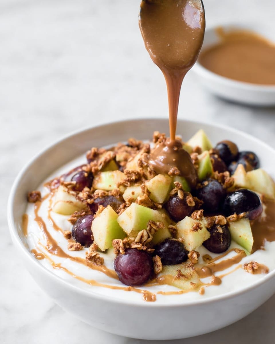 A white bowl filled with a smooth layer of creamy white yogurt as the base. On top, there is a layer of mixed chopped fruit pieces including dark purple grapes and light green apple chunks, sprinkled with crunchy granola bits. Swirling around and partially over the fruit and granola is a thick, smooth brown sauce being drizzled from a spoon held above the bowl. All is set against a white marbled surface with a small white plate blurred in the background also holding some of the brown sauce. photo taken with an iphone --ar 4:5 --v 7