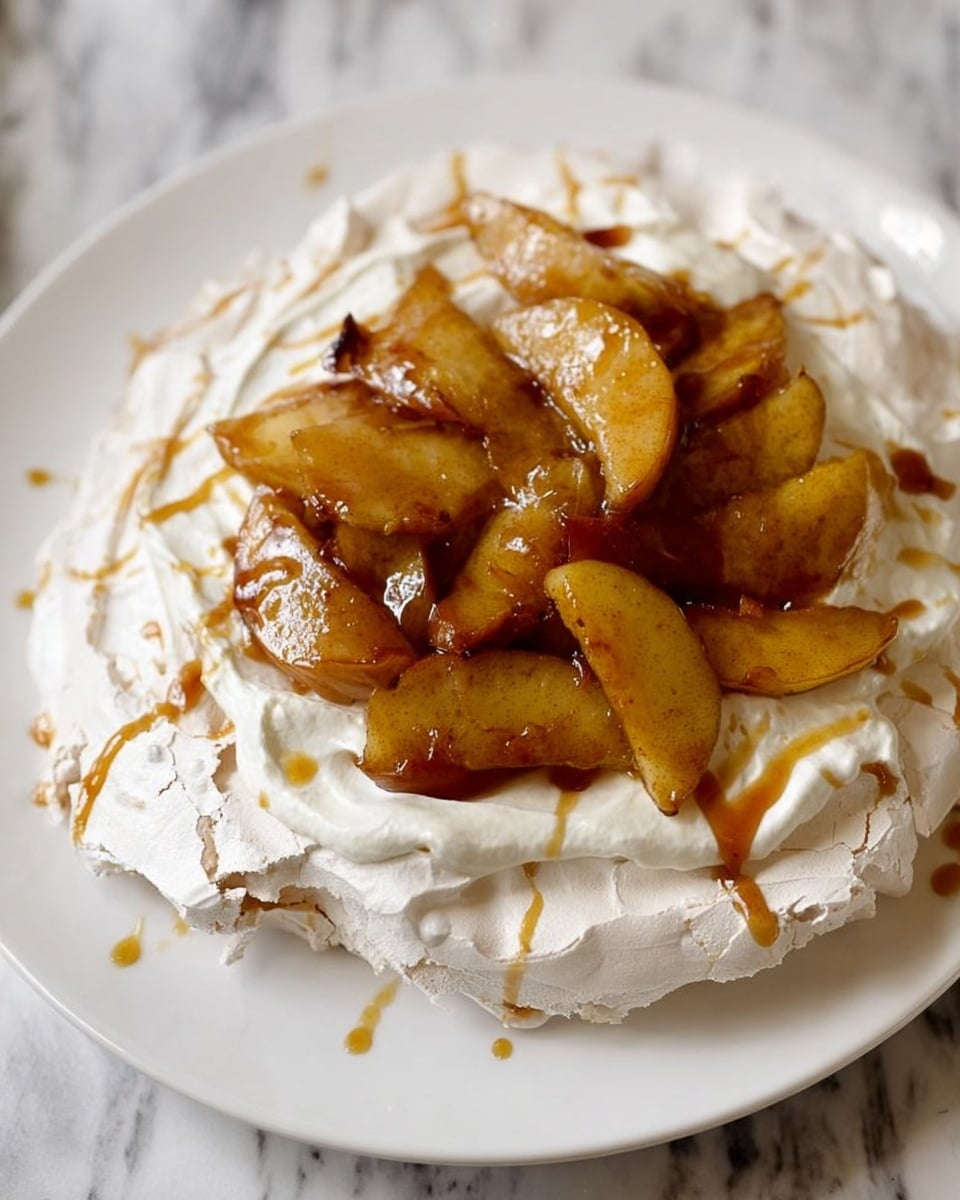 A white plate holds a single-layer pavlova with a base of light, crisp meringue that is slightly cracked and airy. On top of the meringue is a thick layer of smooth, white whipped cream spread unevenly. Sitting on the whipped cream are soft, caramelized apple slices with a golden-brown color and glossy texture, arranged loosely at the center. A light drizzle of caramel sauce coats the apples and parts of the whipped cream, adding a rich amber shine to the dessert. The background is a white marbled surface. photo taken with an iphone --ar 4:5 --v 7