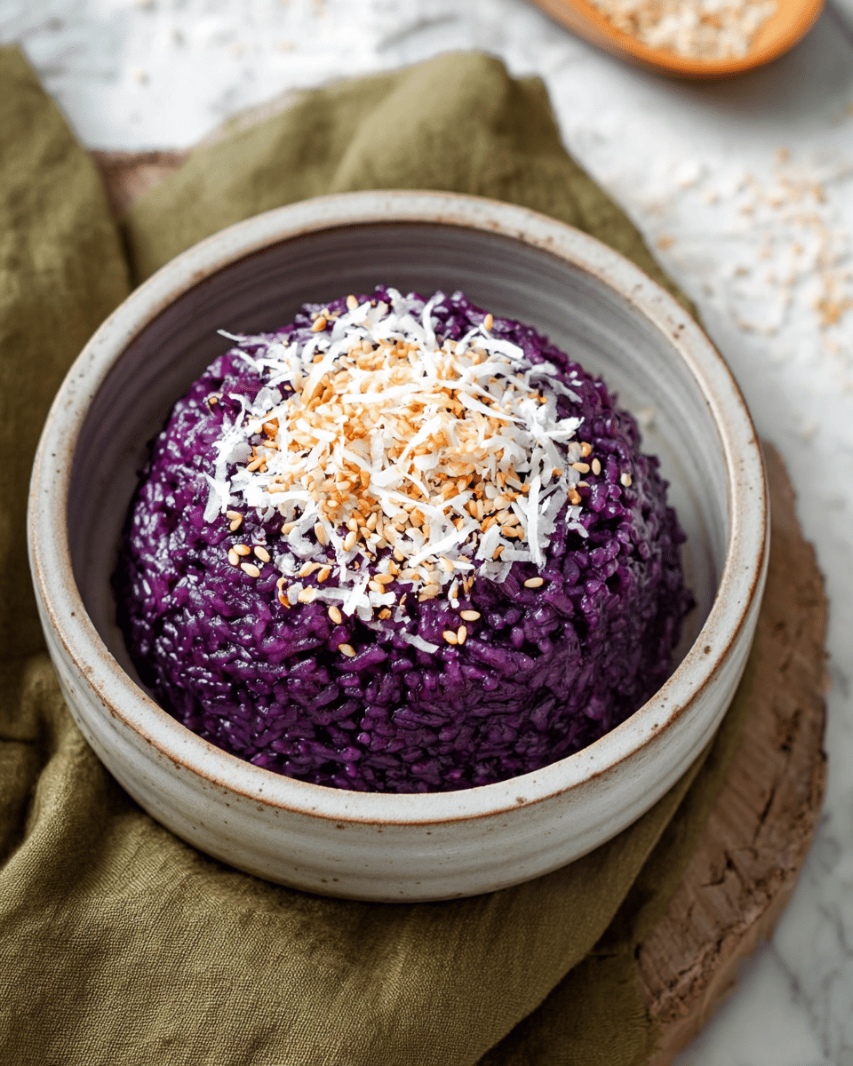 A bowl of purple sticky rice shaped into a dome with a glossy, slightly wet texture inside a white rustic ceramic bowl. The top layer of the rice is sprinkled with shredded white coconut and light brown sesame seeds, adding texture contrast. The bowl is placed on a soft olive-green textured cloth, all set against a white marbled surface with some grains of rice scattered around. Photo taken with an iphone --ar 4:5 --v 7