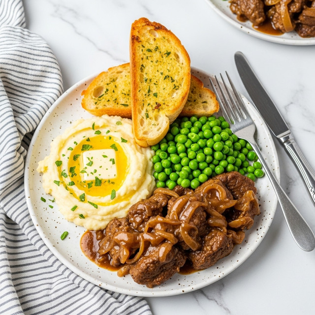The dish is presented on a white speckled plate set on a white marbled surface with a striped cloth underneath, featuring four main layers: a pile of tender brown meat covered in thick brown gravy with visible onion slices on the bottom right, bright green peas clustered next to the meat in the middle right section, creamy mashed potatoes with a small yellow butter pool and sprinkled with chopped green herbs on the left side, and two slices of toasted golden-brown garlic bread placed diagonally on top of the peas and potatoes at the top right. A silver fork and knife rest beside the plate on the right. In the background, another plate with the same food is partially visible. Photo taken with an iphone --ar 4:5 --v 7