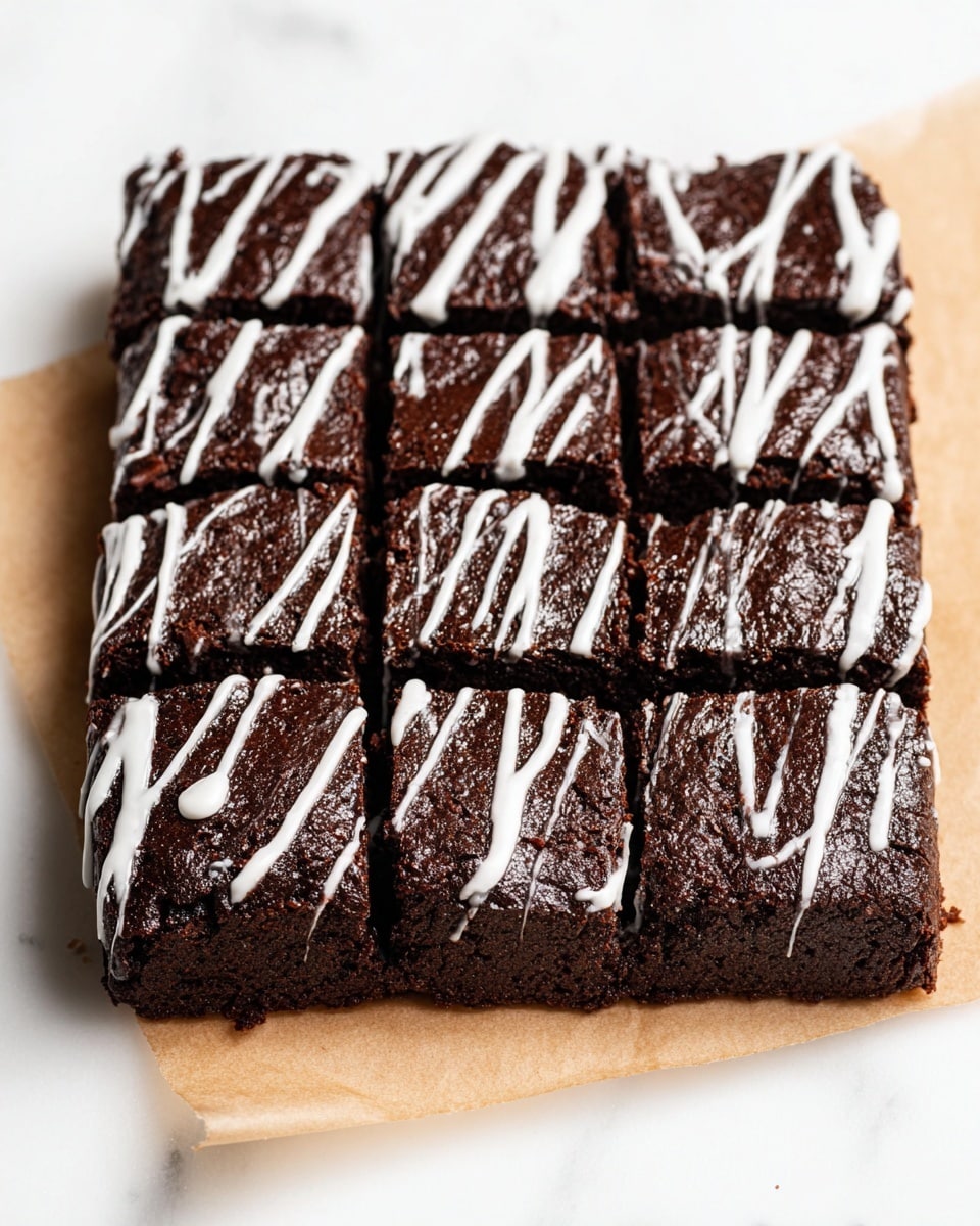 A rectangular chocolate brownie is cut into nine square pieces, arranged tightly in three rows and three columns, with a moist, slightly rough texture. The brownie is dark brown and sits on a piece of light brown parchment paper on a white marbled surface. White icing is drizzled unevenly across the top and down the sides of the brownies, creating thin and thick lines running vertically. The edges are sharp and the surface slightly cracked, showing softness inside. Photo taken with an iphone --ar 4:5 --v 7