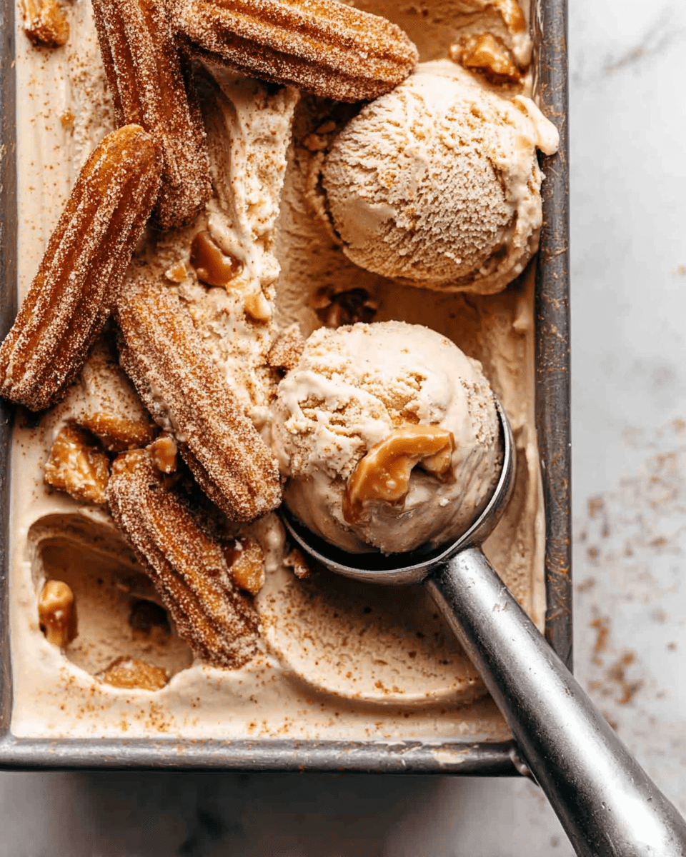 The image shows a metal tray filled with light brown ice cream that has a creamy texture with small chunks of caramel-colored pieces mixed in. On top of the ice cream, there are several churros coated in golden brown sugar and cinnamon, adding a crunchy texture. One scoop of ice cream is held in a metal ice cream scooper positioned near the bottom right corner. The background is a white marbled texture. photo taken with an iphone --ar 4:5 --v 7