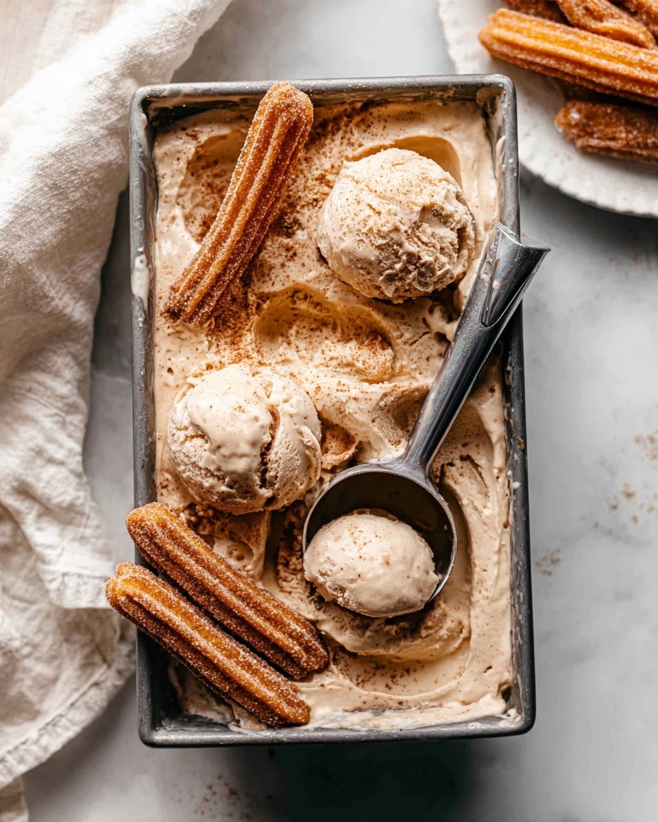 The image shows a rectangular metal container filled with light brown ice cream that has a creamy, slightly melted texture. There are three large scoops of the ice cream placed on top, showing a smooth yet chunky surface with some visible mix-ins. Two ridged, caramel-colored churros, dusted with cinnamon sugar, are partially submerged in the ice cream at opposite corners. A metal ice cream scooper is scooping one ball of ice cream near the top center of the container. The container is placed on a white marbled texture with a soft white cloth nearby, and part of a white plate with churros is visible in the corner. photo taken with an iphone --ar 4:5 --v 7
