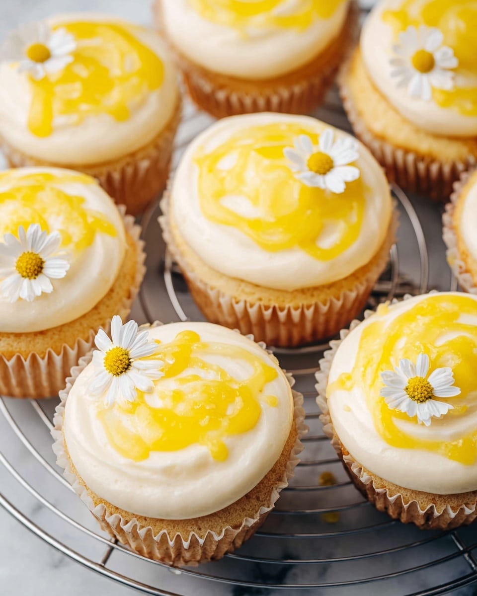 The image shows several lemon cupcakes arranged closely on a round metal cooling rack, placed on a white marbled surface. Each cupcake has a light golden base, topped with a smooth, creamy white frosting layer that looks soft and fluffy. On top of the frosting, there are irregular swirls of bright yellow lemon glaze adding a shiny texture. Some cupcakes are decorated with small white daisy flowers with yellow centers, placed delicately on the frosting. The colors mainly include creamy white, light golden brown, and vibrant yellow, creating a fresh and inviting look. photo taken with an iphone --ar 4:5 --v 7