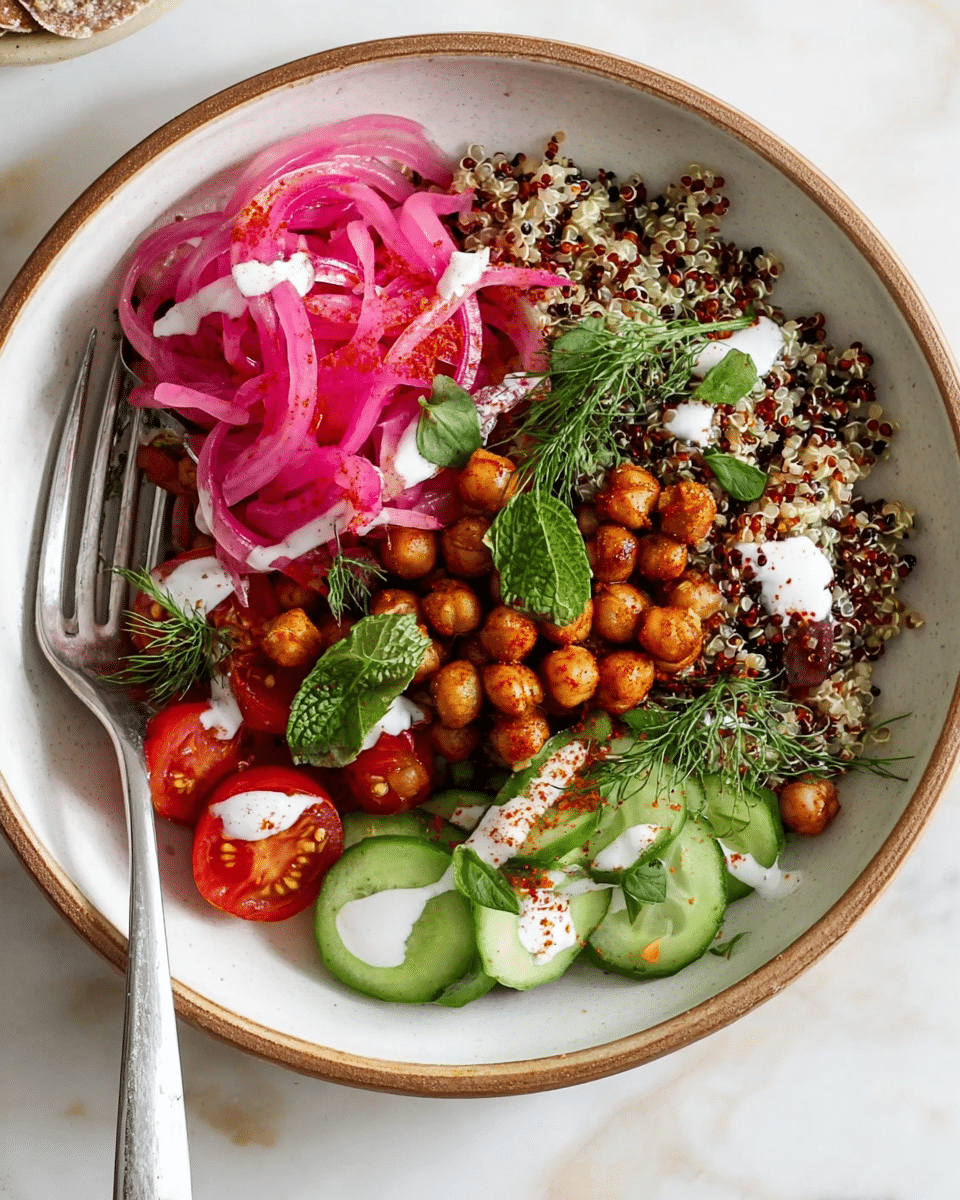 The dish is a colorful grain bowl with four visible layers starting at the base with a bed of cooked quinoa in mixed shades of white, red, and black. On top of the quinoa are small bright green slices of cucumber arranged mainly on one side, a cluster of glossy red cherry tomato halves placed near the bottom, and a pile of golden-brown roasted chickpeas scattered around the center. To the left, there is a neat mound of thin, spiraled pickled red onions with a vibrant pink color. Fresh green herbs like mint leaves and dill sprigs are placed on the right side, adding a fresh look. The whole bowl is drizzled with a white creamy sauce and light specks of reddish spice sprinkled over it. A silver fork rests on the bottom left side inside the bowl, which is white with a rough light brown rim, placed on a white marbled surface. photo taken with an iphone --ar 4:5 --v 7