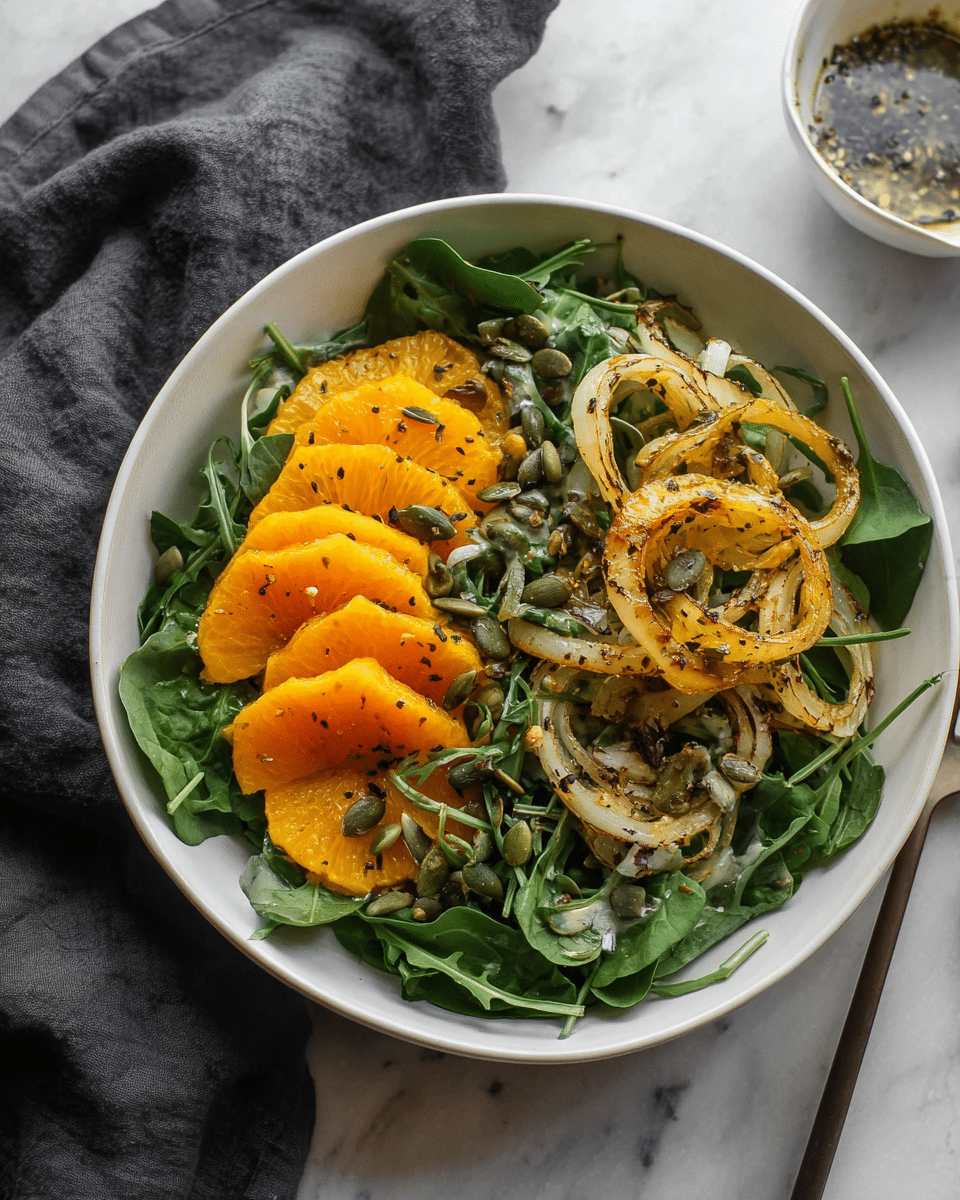 A white bowl filled with a fresh salad sits on a white marbled surface. The salad has a base layer of dark green spinach and arugula leaves covering the whole bowl. On top, there are two main sections: on the left side, bright orange slices are arranged neatly, slightly overlapping each other. On the right side, there are golden-brown roasted onion rings with a slightly crispy texture. Scattered evenly across the salad are small green pumpkin seeds and tiny bits of chopped white onion. The salad is lightly sprinkled with black pepper and some small green herbs. A dark gray cloth is partially visible in the upper left corner, and a small white bowl with dressing or sauce is in the top right. Photo taken with an iphone --ar 4:5 --v 7