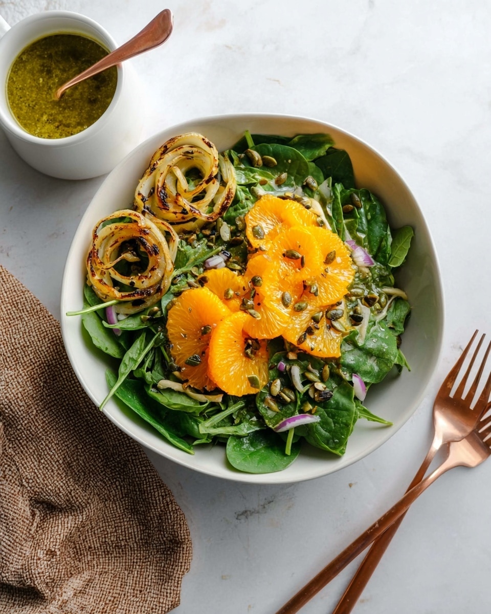 A white bowl filled with a leafy green salad sits on a white marbled surface, layered with fresh spinach leaves as the base. On top, there are two clusters of bright orange slices, evenly placed apart, with small chopped red onion sprinkled over. To one side of the bowl, grilled fennel rings with a slight char add texture and a golden brown color. Scattered pumpkin seeds lightly cover the spinach. Nearby, a white cup holds a greenish-yellow sauce with a copper spoon resting inside. Two rose gold forks lie next to the bowl on the right side, complementing the clean and fresh look of the dish. Photo taken with an iphone --ar 4:5 --v 7