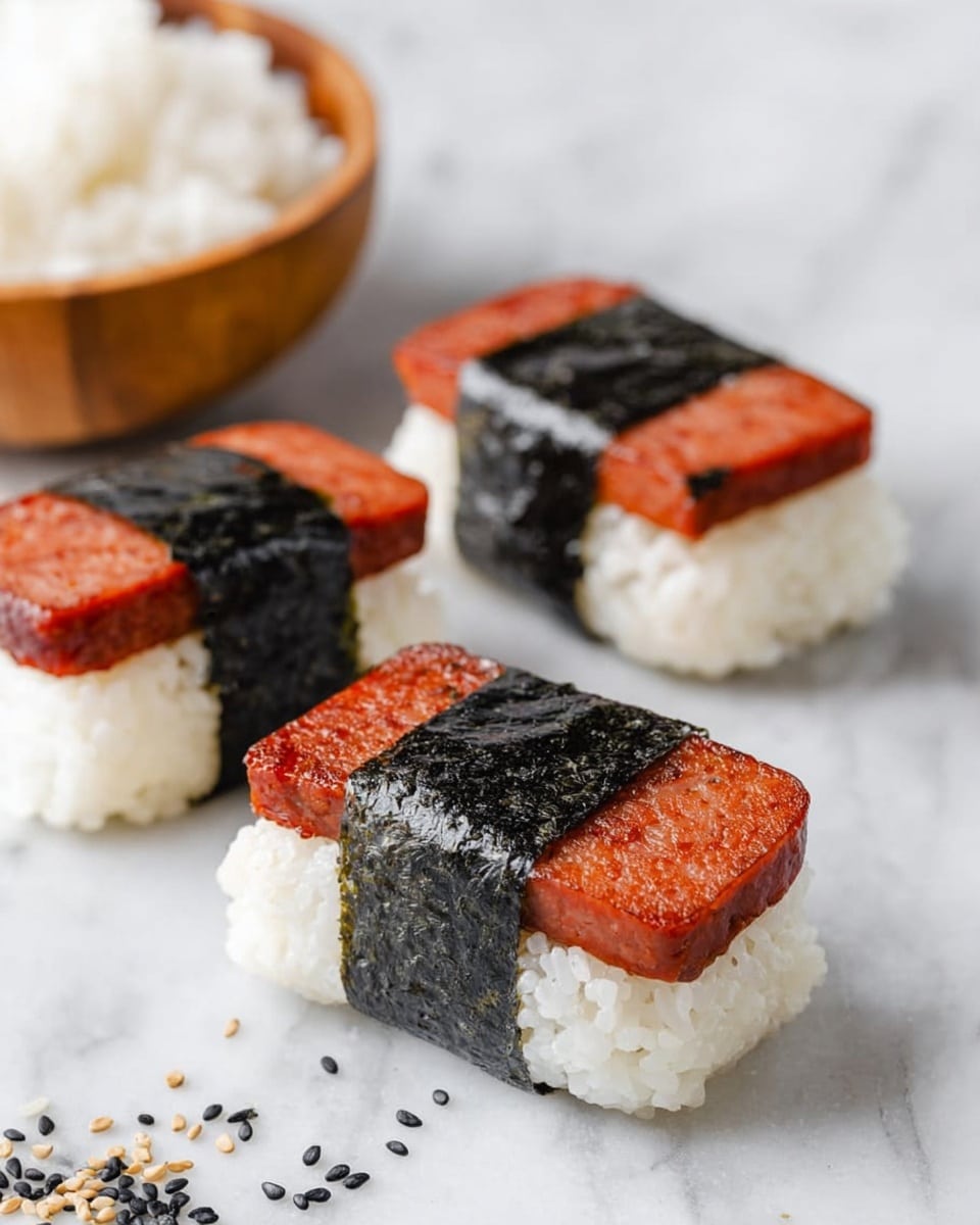 The image shows three pieces of spam musubi arranged on a white marbled surface. Each piece has three layers: the bottom layer is white rice with a slightly sticky texture, the middle layer is a rectangular block of reddish-brown grilled spam, and the top layer is a shiny, black seaweed strip wrapped around the center holding the spam and rice together. Small black and white sesame seeds are scattered around the musubi pieces. In the background, there is a round wooden bowl filled with white rice, slightly out of focus. Photo taken with an iphone --ar 4:5 --v 7
