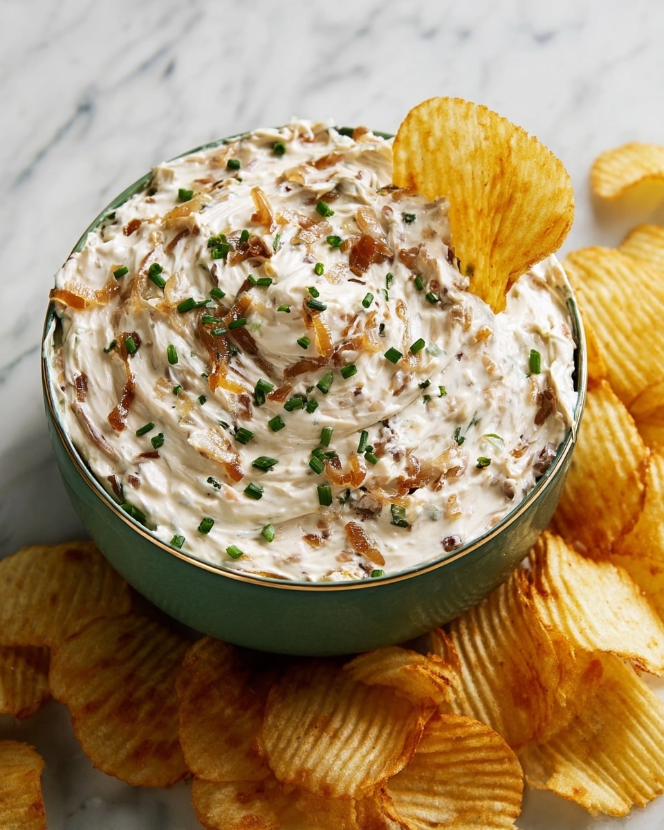 A white bowl filled with a creamy dip that has visible brown caramelized onion pieces mixed throughout, creating a swirled texture. Small green chopped chives are sprinkled on top evenly, adding a fresh color contrast. One ridged potato chip is dipped into the creamy mixture, standing out with its golden-yellow color and wavy texture. More potato chips surround the bowl on a white marbled surface, enhancing the snack presentation with their light and crunchy look. photo taken with an iphone --ar 4:5 --v 7