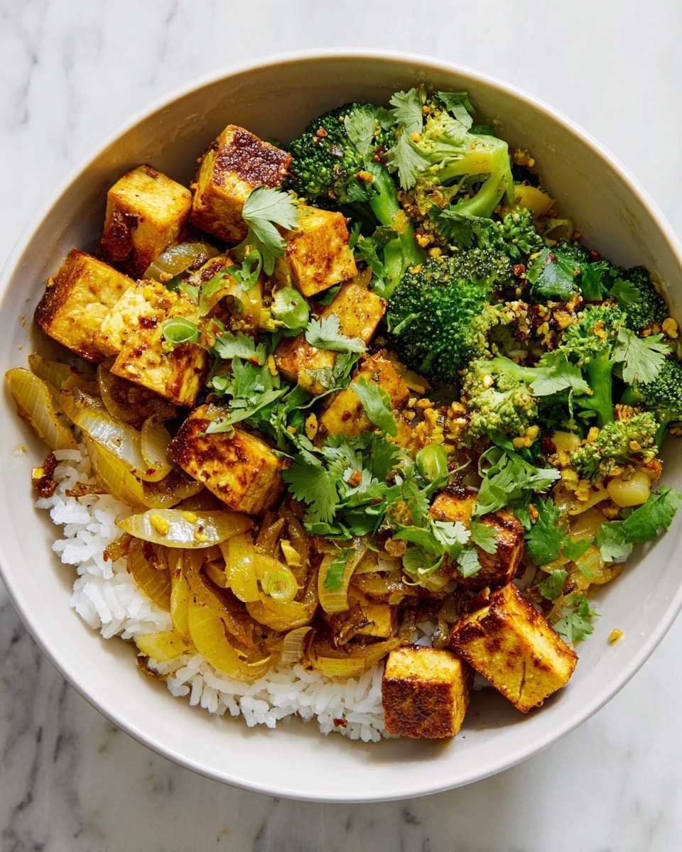 A white bowl filled with three layers: the bottom layer is fluffy white rice, the middle layer has golden brown cubes of cooked tofu mixed with cooked light yellow onion slices, and the top layer includes bright green broccoli florets and fresh cilantro leaves scattered on top. The tofu and vegetables have a slight oily, glossy texture with visible specks of seasoning, placed on a white marbled surface. photo taken with an iphone --ar 4:5 --v 7