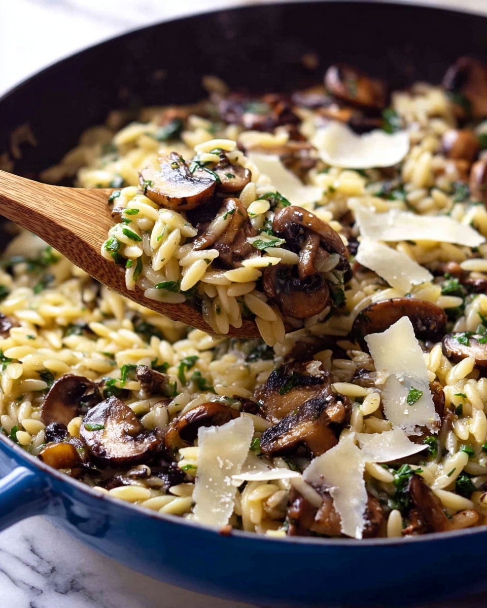 A close-up view of a blue pan filled with cooked orzo pasta mixed with sautéed mushrooms and chopped green herbs. The orzo is cream-colored and shiny, while the mushrooms are browned and slightly crispy on the edges, scattered evenly throughout the dish. Thin, pale shavings of Parmesan cheese sit on top, melting slightly into the mix. A wooden spoon lifts a portion of the pasta, mushrooms, and herbs, showing the mixture's texture and colors clearly. The pan rests on a white marbled surface. photo taken with an iphone --ar 4:5 --v 7