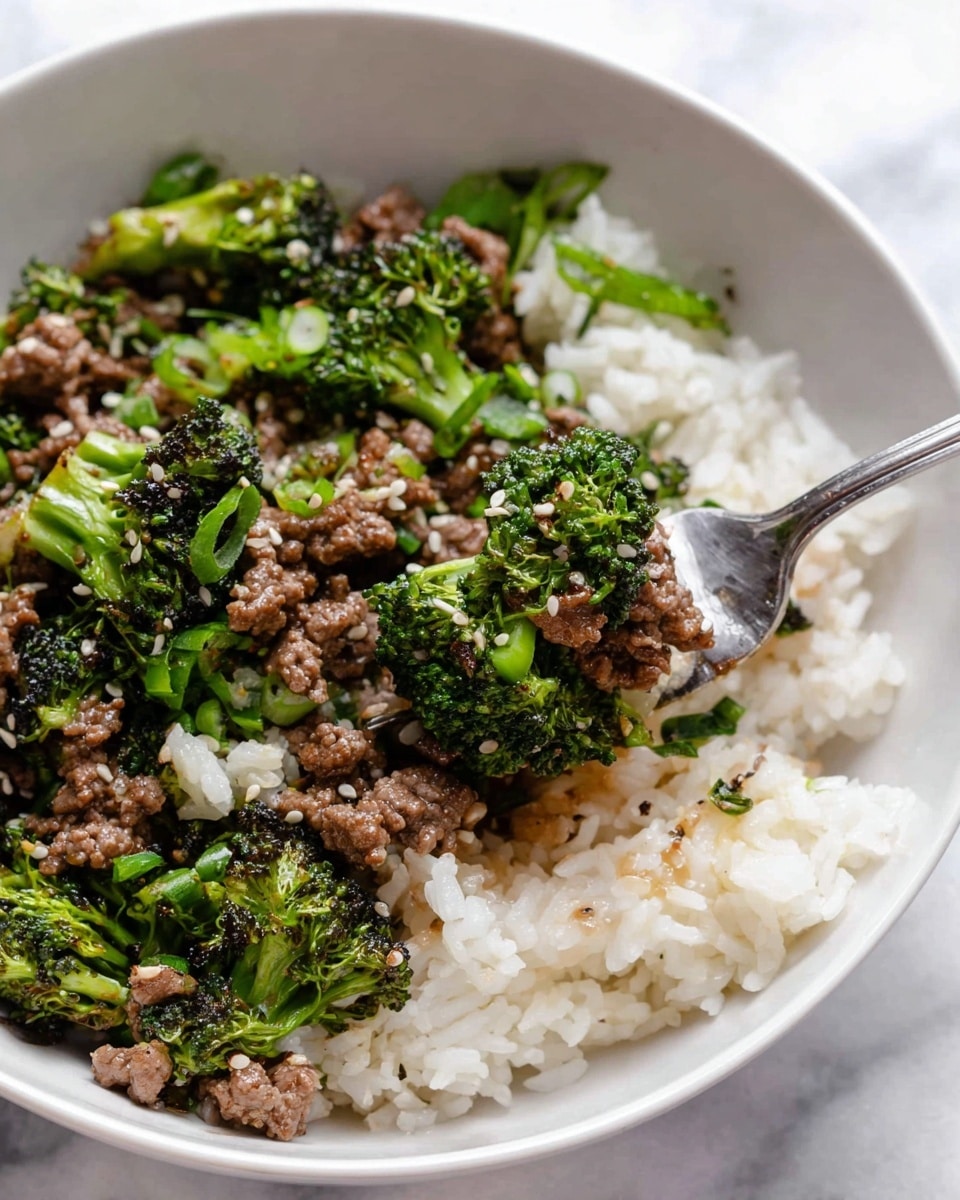 A white bowl holds a dish with two main layers; the bottom layer is fluffy white rice with some pieces of chopped green onions and sesame seeds sprinkled on top, giving light green and black color bits. The top layer is a mix of cooked ground beef and bright green broccoli pieces, cooked to a soft texture with some small bits of onions visible. A silver fork is digging in, lifting a portion that includes a chunk of broccoli and some rice, the food looking well mixed but still showing the distinct layers. The bowl sits on a surface with a white marbled texture. photo taken with an iphone --ar 4:5 --v 7
