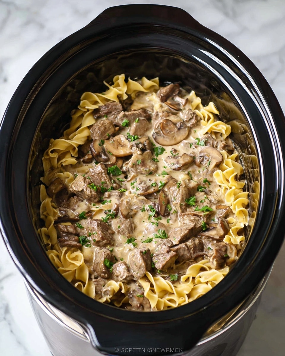A white plate holds a creamy mushroom and beef liver dish layered with wide, pale yellow egg noodles as the base, topped with large, tender brown liver pieces and slices of cooked mushrooms covered in a glossy, light brown sauce. Small green parsley sprinkles are scattered on top, adding contrast. The plate sits on a white marbled surface with a beige cloth underneath. In the background, a shallow bowl with green herbs and a reflective silver kitchen timer are partially visible. Photo taken with an iphone --ar 4:5 --v 7