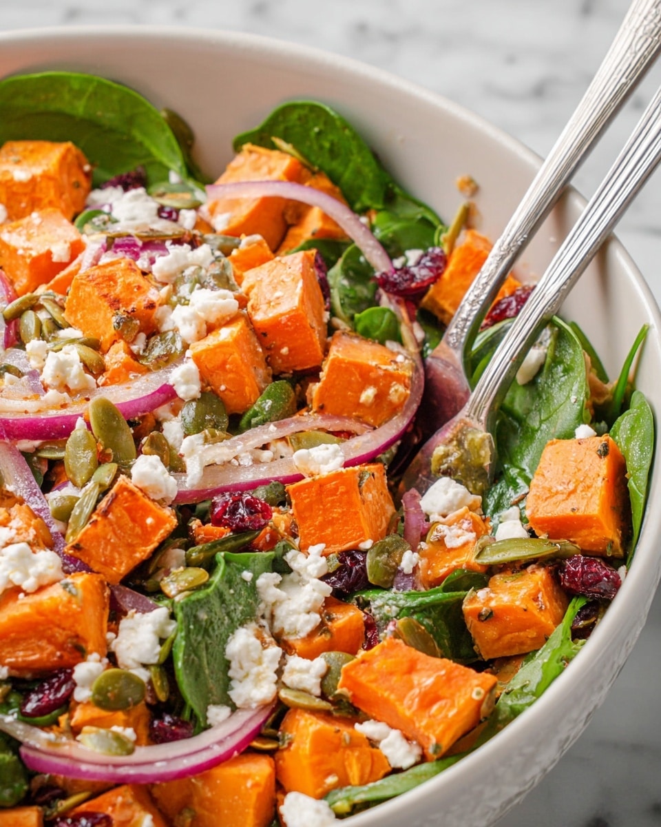 A close-up view of a white bowl filled with a colorful salad made of four main layers: bright orange cubes of roasted sweet potatoes scattered throughout; fresh green spinach leaves layered underneath and mixed in; thin slices of light purple red onions spread evenly; and small chunks of white feta cheese sprinkled on top. There are also small green pumpkin seeds and dark red dried cranberries mixed among the layers, adding texture and color. Two silver salad forks rest inside the bowl, partially submerged in the salad. The bowl sits on a white marbled surface. photo taken with an iphone --ar 4:5 --v 7