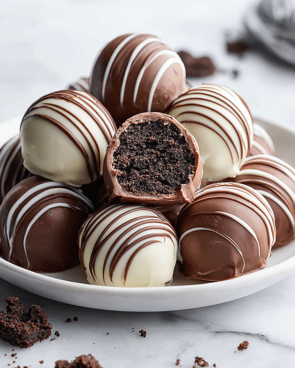 A white plate holds a small pile of round truffles, each with two main layers: a smooth outer chocolate shell and a dark, dense center. Some truffles have a white chocolate shell with thin dark chocolate stripes drizzled on top, while others have a dark chocolate shell with thin white chocolate stripes. The textures of the shells are glossy and smooth. One truffle is cut in half at the center, showing the dark, moist, crumbly inner layer, surrounded by a thin chocolate coating. The plate sits on a white marbled surface with some small cookie crumbs scattered nearby. Photo taken with an iphone --ar 4:5 --v 7