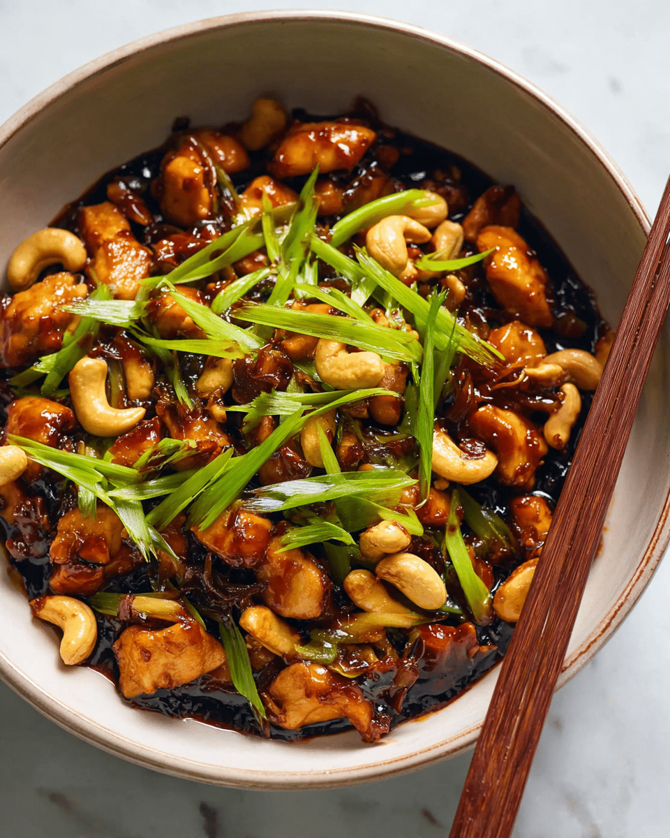 A close-up of a bowl filled with a glossy stir-fry dish showing three main layers: the bottom layer is a dark, thick sauce; on top of it are bite-sized, golden-brown chicken pieces mixed with pale cashew nuts and small dark brown bits that look caramelized; the top layer is bright green, thinly sliced scallions scattered over the dish. The bowl is white, and a pair of brown chopsticks rest on its edge, all set against a white marbled texture. Photo taken with an iphone --ar 4:5 --v 7