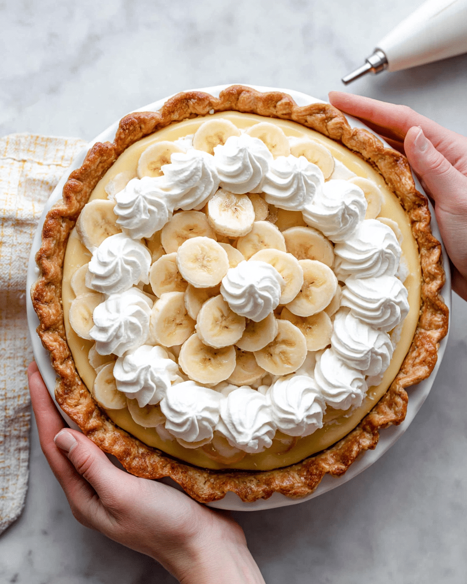 A close-up view of a banana cream pie held by a woman's hands, showing a golden brown, flaky pie crust edge on a white pie plate. Inside the pie, there is a smooth, light yellow cream layer as the base. On top of the cream, there are swirled dollops of white whipped cream arranged in a circular pattern near the crust and in the center, topped with evenly spaced light yellow banana slices that have a soft texture and visible seeds. The pie rests on a white marbled surface with a white piping bag nearby. Photo taken with an iphone --ar 4:5 --v 7