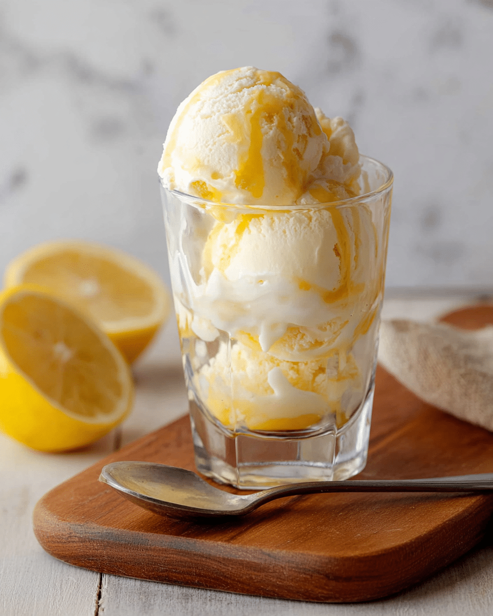 A clear glass cup sits on a wooden board against a white marbled texture background, filled with three scoops of ice cream stacked on top of each other. The ice cream has a creamy white base with bright yellow swirls throughout, giving it a smooth, soft texture with some melting at the edges. To the left, there is a half-cut lemon resting on the board, adding a fresh yellow contrast. A silver spoon lies next to the board on the white marbled surface. Photo taken with an iphone --ar 4:5 --v 7