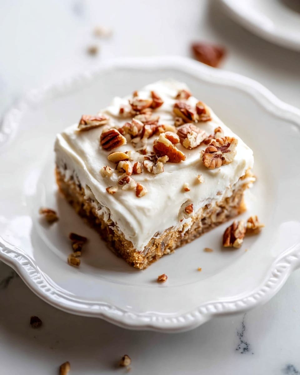 A square piece of cake sits in the center of a white plate with scalloped edges, placed on a white marbled surface. The cake has two main layers: a moist, light brown base layer with small visible bits, and a thick, smooth white cream layer on top. Scattered over the cream layer are medium-sized pieces of pecans that add a textured, brown and tan contrast. A few pecan crumbs are around the plate, enhancing the look of a freshly served dessert. photo taken with an iphone --ar 4:5 --v 7