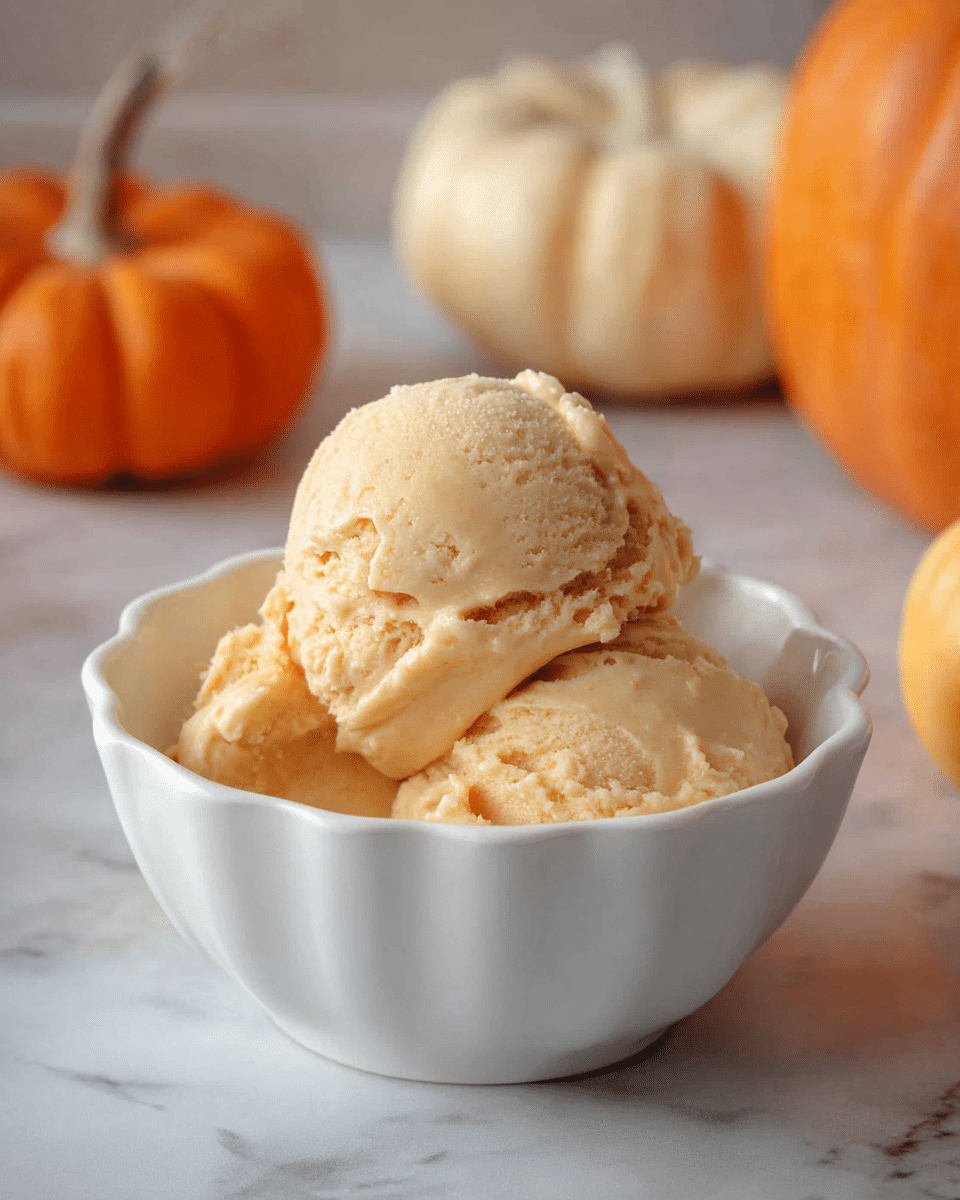 A white scalloped bowl holds two creamy scoops of light orange ice cream with a smooth texture and slight ridges from scooping, placed slightly off-center with a soft focus background featuring small pumpkins in warm orange and pale cream colors on a white marbled surface. photo taken with an iphone --ar 4:5 --v 7