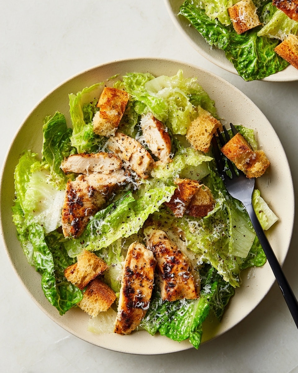 A white plate holds a layer of fresh green romaine lettuce leaves with varying shades from light to medium green, unevenly torn. On top are several pieces of grilled chicken breast, golden-brown with char marks and a slightly shiny surface, arranged in the center. Scattered around are golden, crispy bread croutons with a rough texture. The whole dish is lightly sprinkled with finely grated white cheese and cracked black pepper. A black fork is placed on the right side of the plate, with its prongs slightly resting on the lettuce. The plate sits on a white marbled surface. photo taken with an iphone --ar 4:5 --v 7