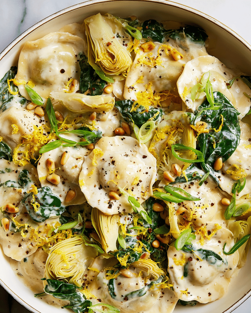 A close-up view of a creamy pasta dish in a large white bowl showing two main layers: the bottom layer is filled with ravioli pieces that are soft and covered in a thick white cream sauce, sprinkled with cracked black pepper; the top layer has green spinach leaves, pale yellow artichoke hearts, and toasted golden pine nuts, all mixed in with the pasta and cream; fresh green scallion slices and bright yellow lemon zest are scattered on top, adding a fresh look and texture contrast, all resting on a white marbled surface photo taken with an iphone --ar 4:5 --v 7