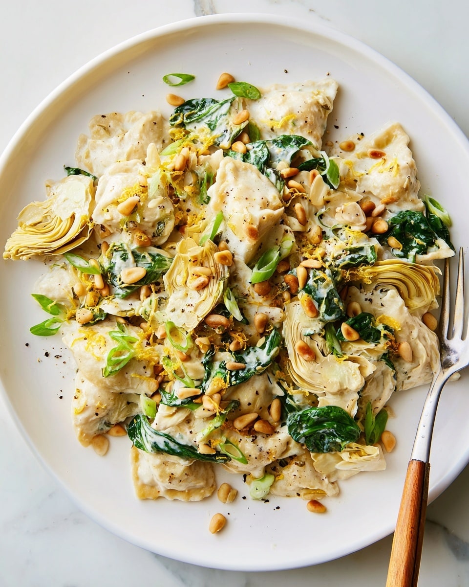 The dish is served on a white plate placed on a white marbled surface, consisting of multiple layers starting with soft, cream-colored pasta pieces that are covered in a light, creamy white sauce. Mixed within the pasta are vibrant green spinach leaves and slightly translucent artichoke hearts. Scattered on top are golden-brown pine nuts, small green onion slices, and a sprinkle of freshly ground black pepper and lemon zest, adding texture and color contrast. There is a fork with a wooden handle resting on the side of the plate. Photo taken with an iphone --ar 4:5 --v 7
