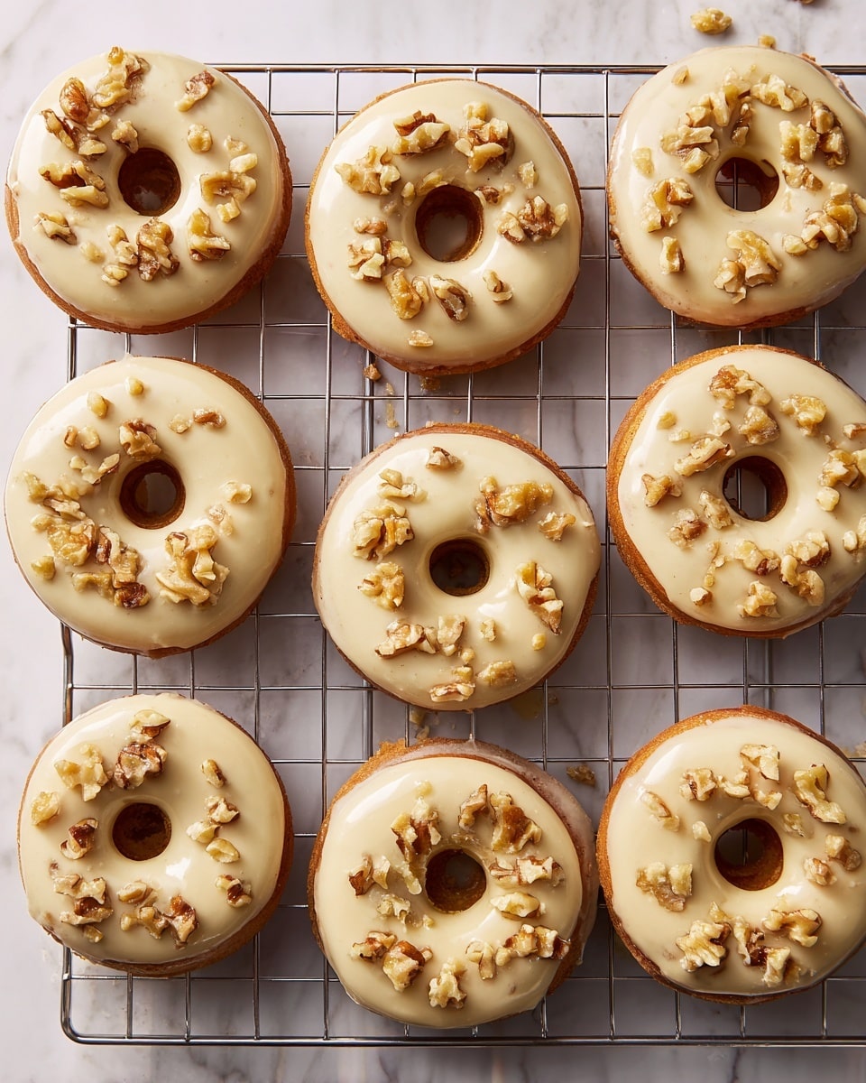 There are ten round donuts arranged in three rows on a metal cooling rack, placed on a white marbled surface. Each donut has one layer of smooth, light beige icing covering the top, with uneven small pieces of chopped walnuts scattered over the icing. The donuts are golden brown, visible around the edges below the icing. Photo taken with an iphone --ar 4:5 --v 7
