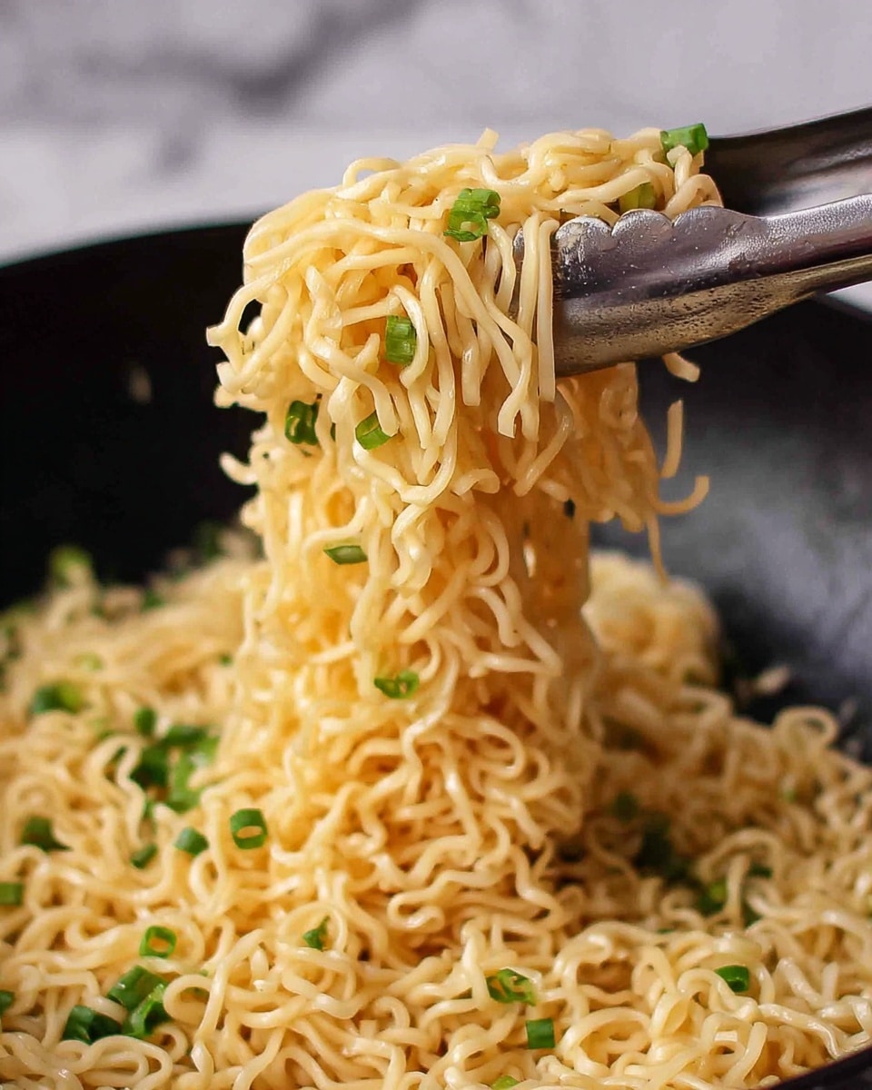 The image shows a close-up of cooked yellow noodles lifted by silver tongs, with small pieces of chopped green onions scattered throughout the noodles. The noodles look soft and shiny, hanging in a loose bundle above a black pan filled with more noodles and green onions. The background features a white marbled texture, giving a clean and simple look. Photo taken with an iphone --ar 4:5 --v 7