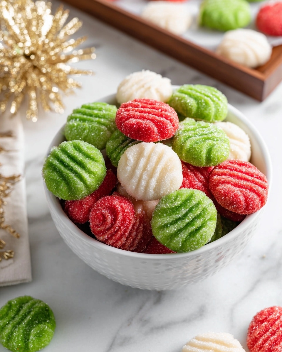 A white bowl filled with small round cookies in three colors: bright green, red, and white. Each cookie has a pattern of fork marks on top and is sprinkled with sugar crystals, giving a slightly shiny and textured look. The green and red cookies dominate the bowl, with a few white ones peeking through. Some green cookies are also scattered beside the bowl on a white marbled surface. In the background, there is a wooden tray with more green cookies on white parchment paper and a golden sparkly decoration to the left. photo taken with an iphone --ar 4:5 --v 7