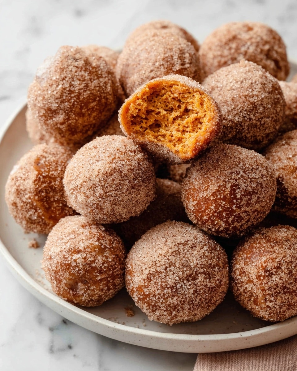 A white plate holds many round doughnut holes covered in a light brown sugar and cinnamon coating, giving each piece a textured and slightly grainy surface. One doughnut hole is broken and placed on top, showing an inner soft, moist, and fluffy orange cake-like layer. The plate is set on a white marbled surface that adds a clean and bright background to the warm tones of the dessert. Photo taken with an iphone --ar 4:5 --v 7