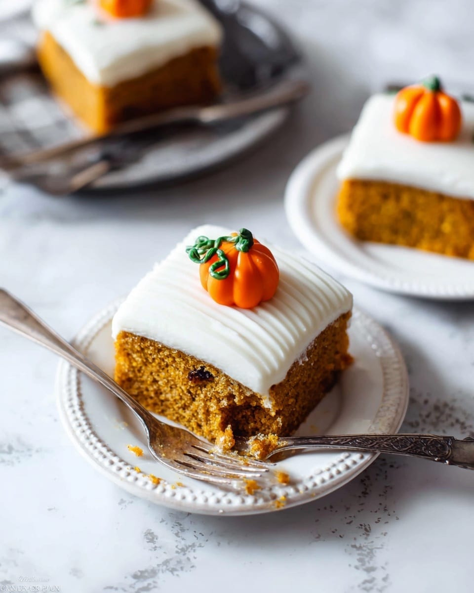 The image shows a square slice of cake on a white plate with a decorative edge, sitting on a white marbled surface. The cake has two layers: the bottom layer is a moist, golden-brown pumpkin cake with small dark bits inside, and the top layer is thick, smooth white frosting with a ridged texture. On top of the frosting is a small, detailed orange pumpkin decoration with a brown stem and green vine made of icing. A silver fork rests on the plate with a bite-sized piece of cake on its tines, with some crumbs scattered nearby. In the background, there is another similar slice of cake on a white plate with a silver fork. Photo taken with an iphone --ar 4:5 --v 7