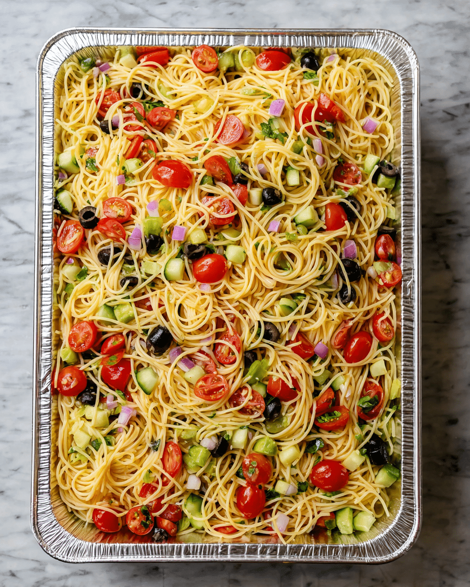 A large rectangular silver tray filled with a colorful pasta salad consisting of thin spaghetti noodles mixed evenly with halved bright red cherry tomatoes, black olive slices, and small diced green bell peppers and cucumbers. There are also small bits of light purple onion scattered throughout. The noodles create a tangled, light yellow base that fills the entire tray, with the vegetables distributed on top and mixed in. The texture looks fresh and slightly oily. The tray is placed on a white marbled surface. photo taken with an iphone --ar 4:5 --v 7