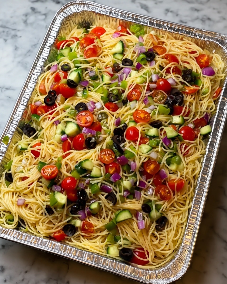 A large aluminum tray filled with a mixed pasta salad. The base layer is thin, light yellow spaghetti noodles, loosely piled and spread evenly across the tray. Mixed throughout are bright red grape tomatoes cut in halves, dark black sliced olives, diced green cucumbers, small pieces of green bell pepper, and bits of purple onion. The colors are vibrant with the fresh vegetables contrasting against the pale noodles. The background is a white marbled texture surface. photo taken with an iphone --ar 4:5 --v 7