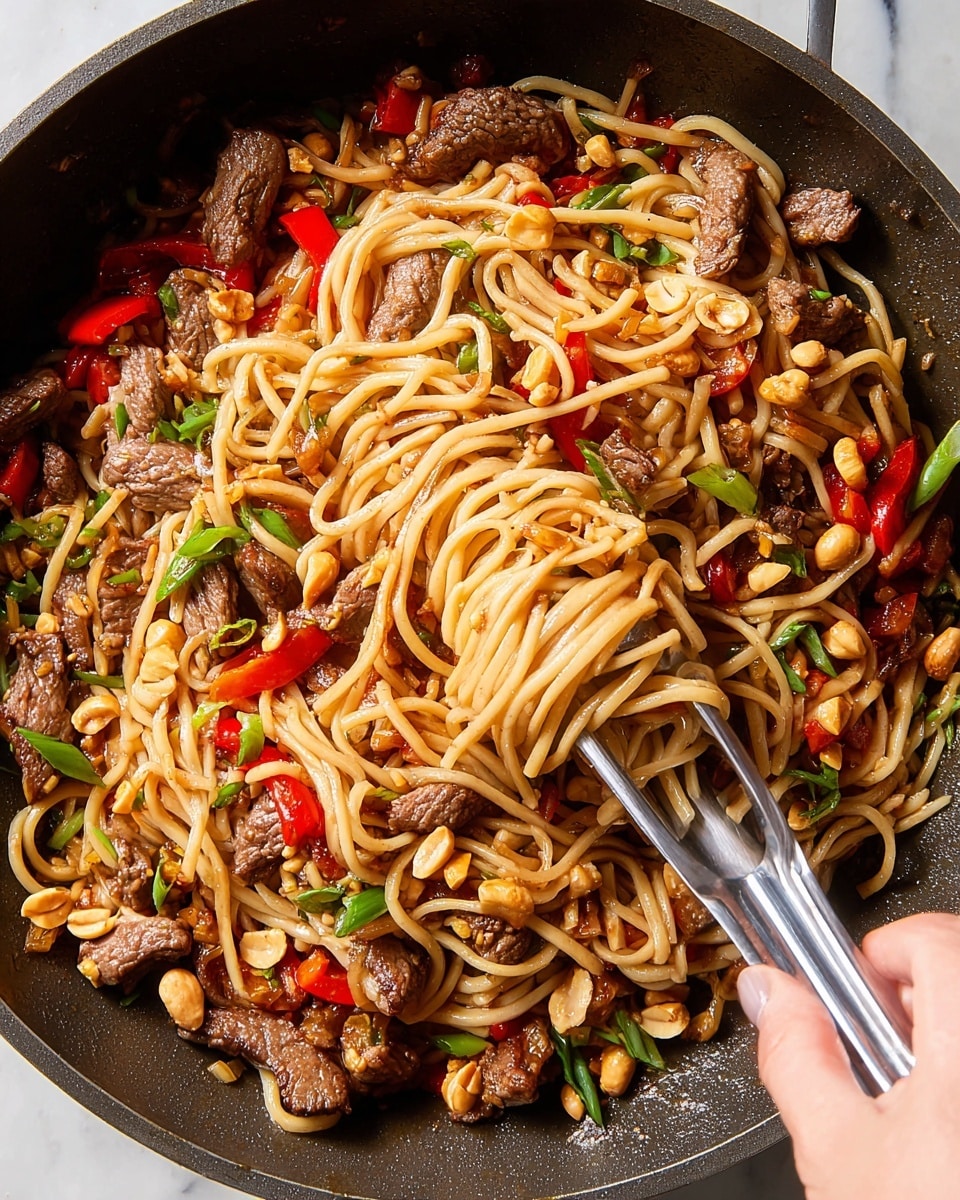 The image shows a close-up of a dark pan filled with stir-fried noodles. The noodles are light brown and mixed with small pieces of cooked beef that have a slightly crispy texture on the edges. Bright red bell pepper chunks are scattered throughout the dish, adding color contrast. There are also whole peanuts and sliced green onions sprinkled on top, giving it a varied texture and green and tan tones. A silver tong held by a woman's hand is lifting some noodles in the center, creating a twisting motion. The background is a white marbled texture. Photo taken with an iphone --ar 4:5 --v 7
