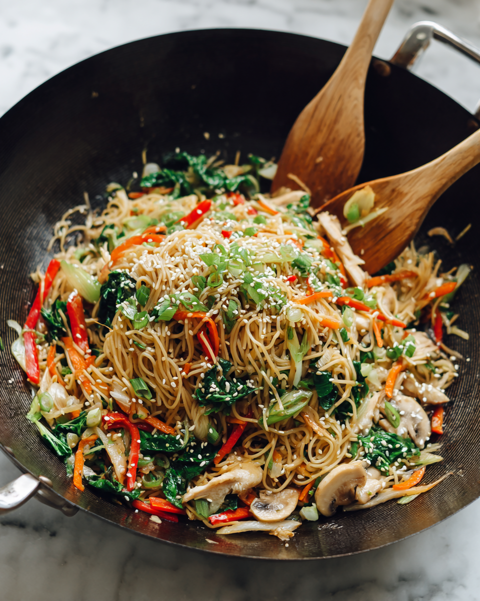 A close-up view of a dark wok filled with stir-fried noodles and vegetables, showing three main layers: the bottom layer includes light brown thin noodles, the middle layer features bright green leafy vegetables and chopped scallions, and the top layer has thin orange carrot strips, red pepper slices, pieces of white chicken, and small brown mushrooms, all mixed together and sprinkled with white sesame seeds; two light wooden utensils stir the food inside the wok, which sits on a white marbled surface. photo taken with an iphone --ar 4:5 --v 7
