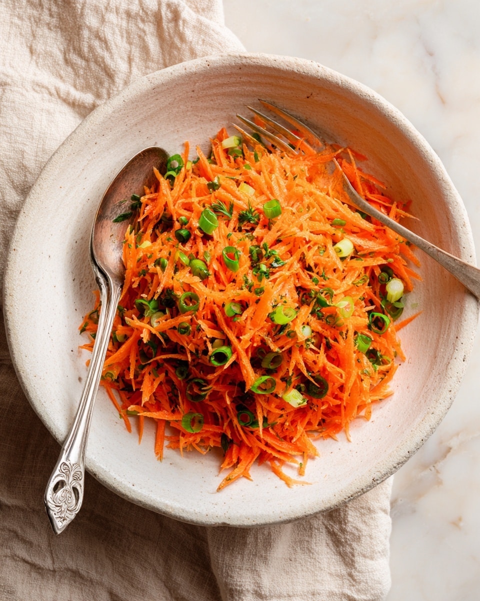 The image shows a bowl filled with a simple carrot salad. The bowl is white and has a rough, natural texture. Inside, there are two layers: a base layer of finely grated bright orange carrots and a mix of sliced green onions scattered evenly throughout. The carrots have a slightly moist and fresh look, while the green onions add a touch of green contrast and freshness. A silver spoon rests inside the bowl on the left side, and a silver fork is on the right, slightly stuck into the salad. The bowl is placed on a soft beige cloth that sits on a white marbled surface. Photo taken with an iphone --ar 4:5 --v 7