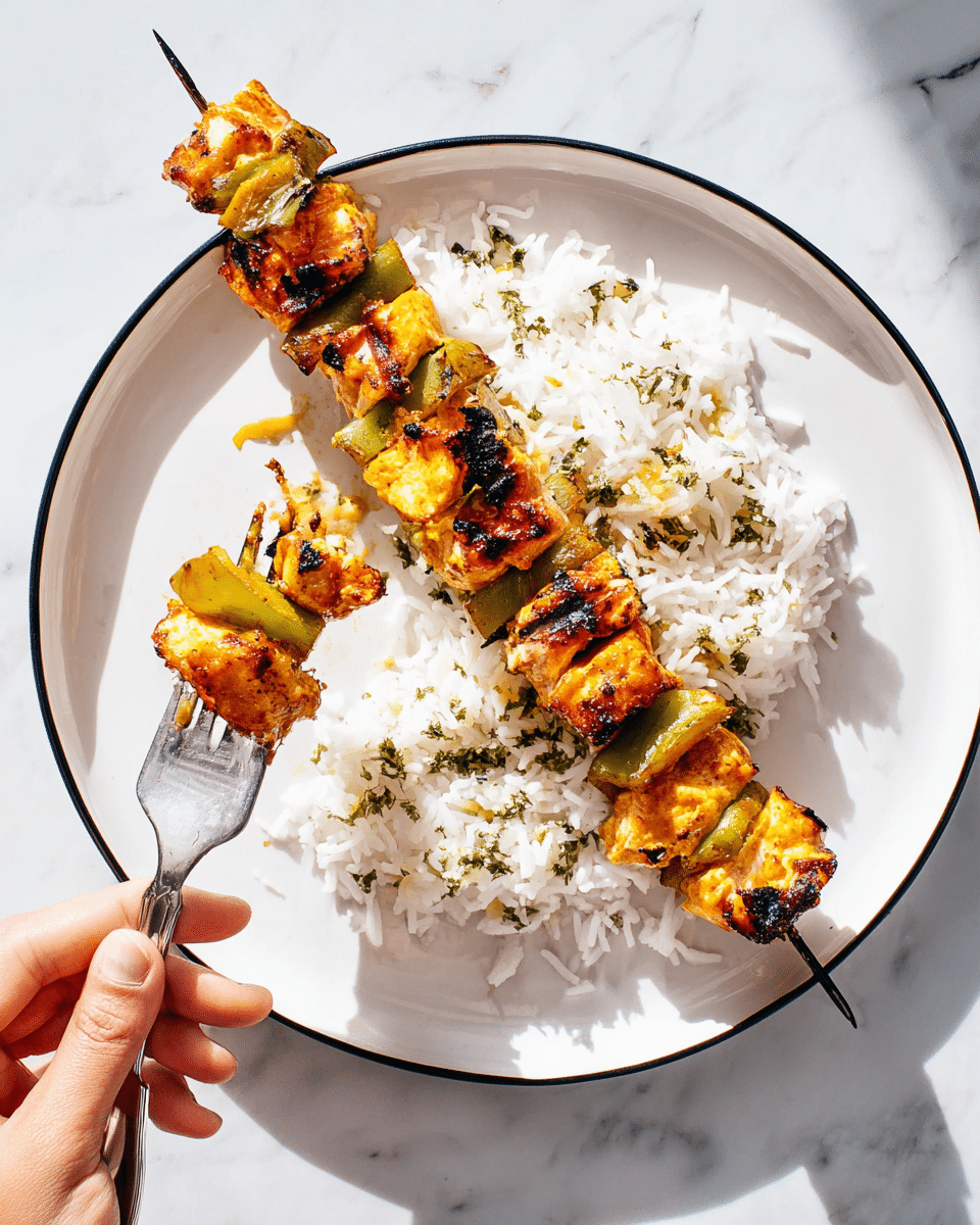 A white plate with a thin black rim holds a serving of white rice, scattered lightly with green herb bits. On top of the rice lie two metal skewers with grilled pieces of orange-yellow marinated chicken and green bell pepper chunks, showing slight char marks. One skewer is whole while the other is being held by a woman's hand using a fork to lift a piece. The background features a white marbled texture surface. The image is bright with natural light highlighting the textures and colors of the food. photo taken with an iphone --ar 4:5 --v 7