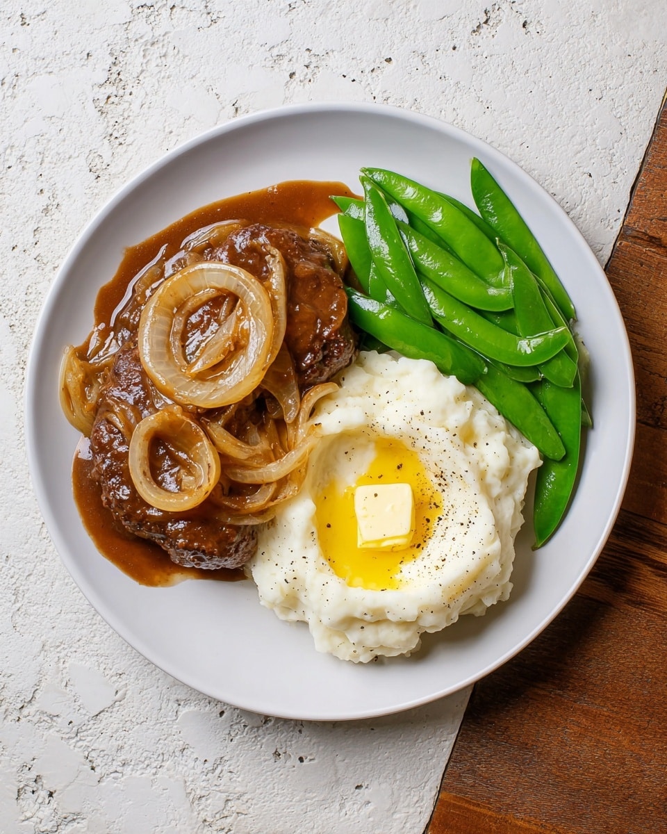 The dish is served on a white plate with three main parts: on the left is a brown beef patty covered in a thick, glossy brown sauce with soft, cooked onion slices on top; in the middle is a creamy mound of white mashed potatoes with a pat of melted yellow butter sitting in a small well in the center, sprinkled with black pepper; on the right side are bright green sugar snap peas with a shiny, slightly oily surface. The plate sits on a white marbled textured surface. photo taken with an iphone --ar 4:5 --v 7