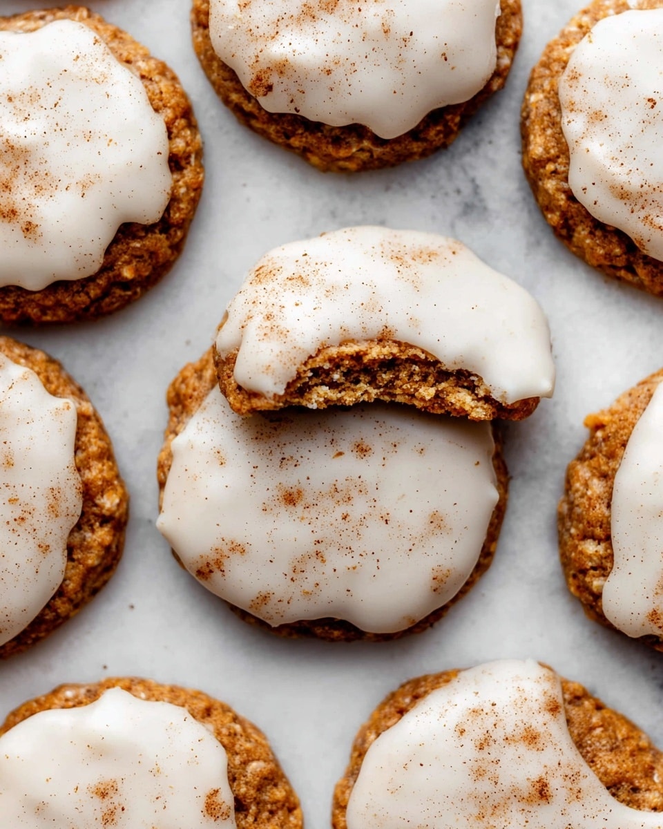 A close-up image of several round cookies laid out on a white marbled surface, each cookie having a golden brown base with a slightly rough, textured appearance. On top, there is one smooth, thick white icing layer that covers most of the cookie surface, with uneven edges allowing some of the cookie base to show through. Light brown spice dusting is sprinkled over the icing, adding a speckled effect. One cookie is partially bitten, showing the soft, moist inside beneath the icing. The cookies are arranged closely but not overlapping. Photo taken with an iphone --ar 4:5 --v 7