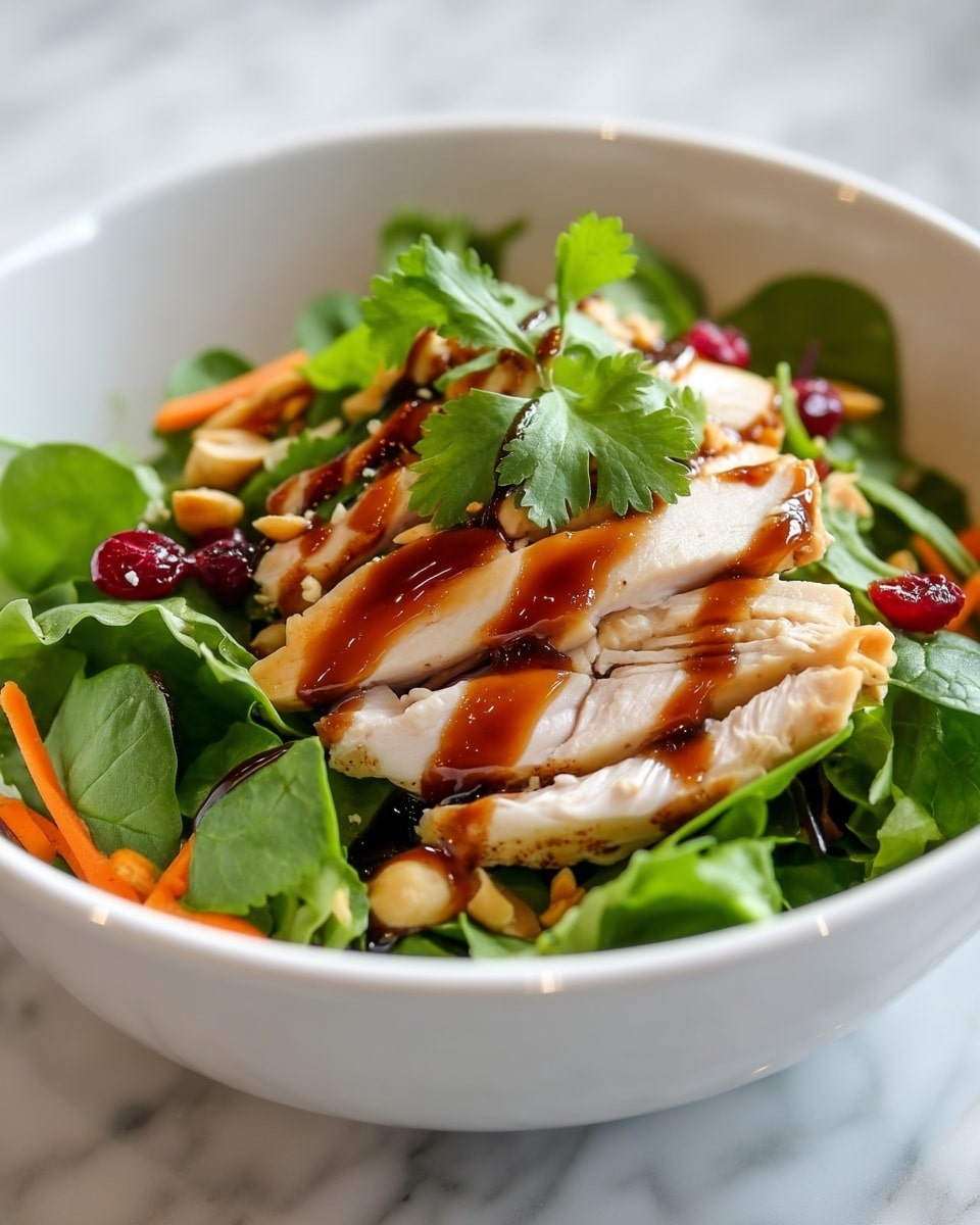 A white bowl holds a fresh salad with a green leafy base of spinach and mixed greens forming the bottom layer. On top, there are thin, bright orange carrot strips and light brown peanuts scattered throughout. The main focus is the third layer, consisting of thick slices of cooked chicken breast, pale with a slight golden brown edge. Over the chicken, there is a glossy dark brown sauce drizzled in lines, along with small red dried cranberries and fresh green cilantro leaves sprinkled on top. The salad looks fresh and colorful with contrasting textures of crunchy nuts and tender chicken. The bowl sits on a white marbled surface. photo taken with an iphone --ar 4:5 --v 7