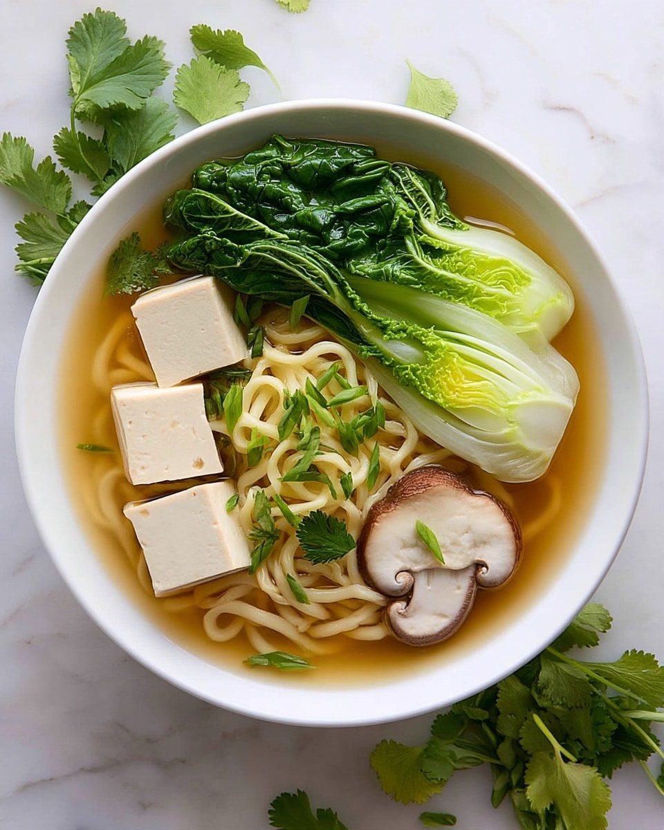 A white bowl contains a clear broth with three large white tofu cubes positioned on the left and bottom right. In the center, a generous nest of light yellow noodles sits surrounded by bright green bok choy leaves and stems toward the top right. Thin slices of light brown shiitake mushrooms with a creamy center are arranged near the noodles on the right and bottom left. Fresh green cilantro leaves and thin slices of green onion are sprinkled across the tofu and noodles, adding vibrant color. The bowl rests on a white marbled surface with some cilantro leaves scattered around and wooden chopsticks lying above the right side of the bowl. Photo taken with an iphone --ar 4:5 --v 7