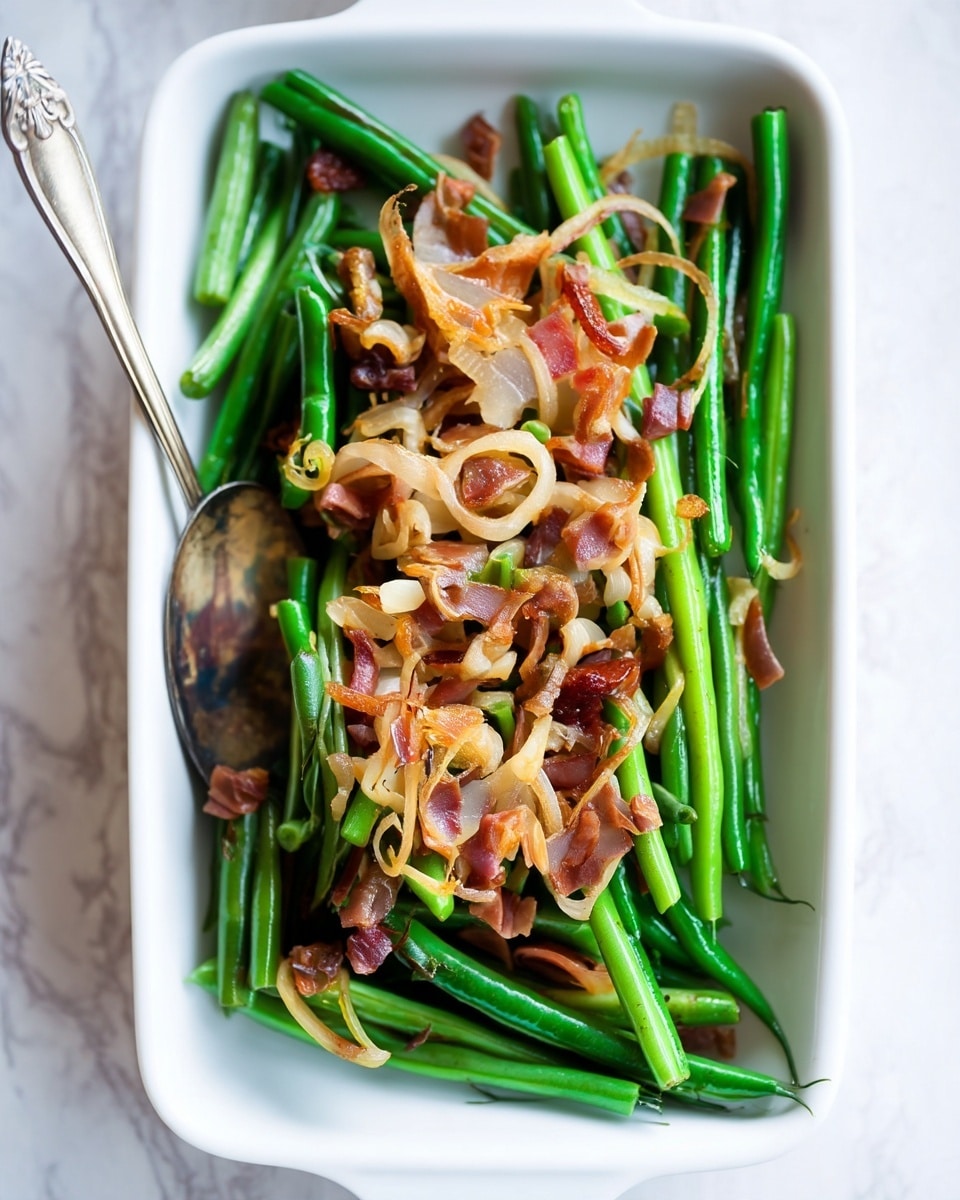 The dish is presented in a white rectangular dish filled with vibrant green beans forming the bottom layer, arranged neatly with a glossy texture. On top of the beans, there is a scattering of crispy, golden-brown sautéed onions that add a soft, curly texture and light color contrast. Mixed throughout the onions are small pieces of reddish-brown prosciutto, adding a rich and slightly crispy texture with a salty appearance. A vintage silver spoon rests on the left side of the dish, slightly buried in the green beans, reflecting light subtly. The background shows a soft, white marbled texture that complements the fresh and warm colors of the dish. Photo taken with an iphone --ar 4:5 --v 7