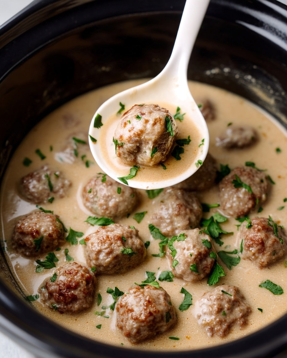 A close-up view of a black pot filled with about twenty small, browned meatballs floating in a thick, creamy light beige sauce garnished with small green parsley pieces scattered on top. In the center, a white ladle holds one meatball partially covered with sauce and some parsley bits. The sauce has a smooth and slightly glossy texture with hints of seasoning. Photo taken with an iphone --ar 4:5 --v 7