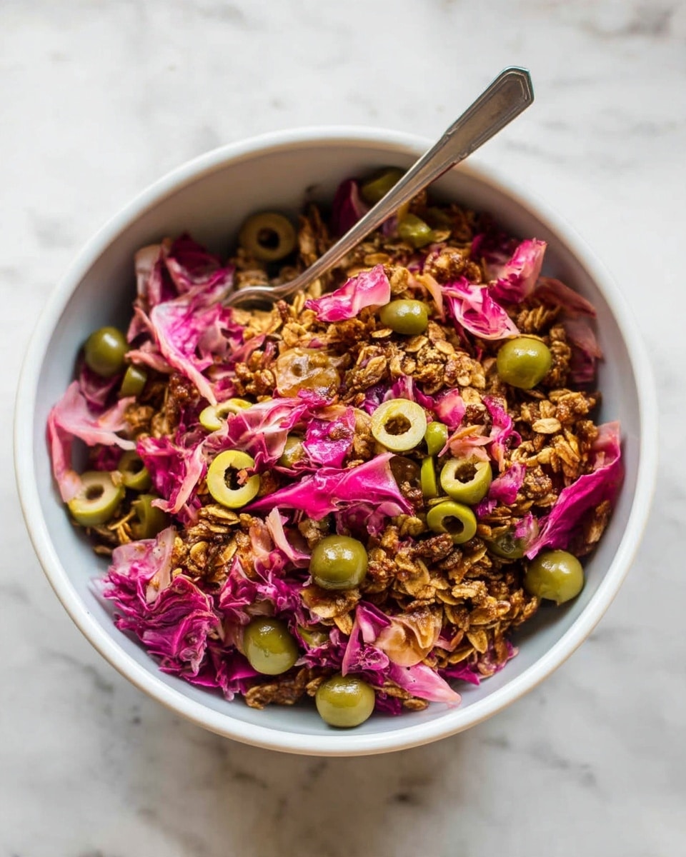 The image shows a white bowl filled with a layered salad on a white marbled surface. The base layer is a mix of crunchy granola or nuts with a golden-brown color and crumbly texture, evenly spread. On top of this is a layer of pink radicchio leaves, torn into pieces with a slightly wilted, delicate texture. Scattered generously over the radicchio are sliced green olives, their smooth rings adding a contrasting bright green color. Two silver forks rest inside the bowl, one slightly inserted into the salad, ready to serve. photo taken with an iphone --ar 4:5 --v 7