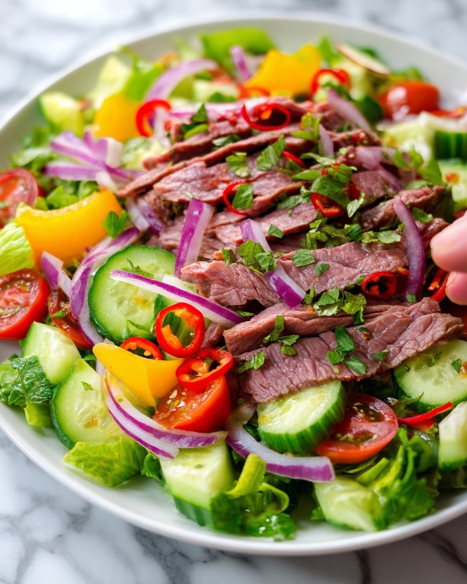 The image shows a fresh salad with several layers of colorful ingredients mixed together. The base layer is made of chopped green lettuce leaves, topped with thin slices of red onion, round cucumber slices, and red chili rings. There are also bright yellow bell pepper strips and halved cherry tomatoes adding pops of color. On top, thin slices of cooked beef with a tender, slightly pink inside are spread evenly across the salad. Finely chopped green herbs are sprinkled over all the layers, giving a fresh and textured look. The salad is presented on a white plate, placed on a white marbled surface. photo taken with an iphone --ar 4:5 --v 7